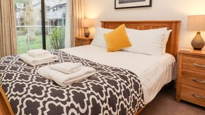 Habitación de hotel con cama, mesita de noche, lámpara, un cuadro en la pared y una ventana con cortinas.