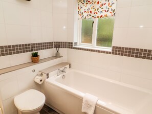 Un baño con bañera, inodoro y una ventana con cortina de hojas.