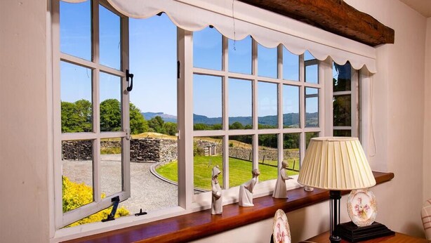 A room with large windows offering a view of a stone wall and greenery.