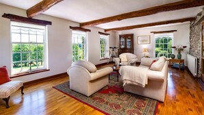 A spacious living room with wooden beams, large windows, and a fireplace.