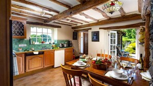 A rustic kitchen with wooden beams, a dining area with a table set for six, and a view of greenery outside.