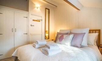 A bedroom with a bed, pillows, a nightstand, a mirror, and a wardrobe.