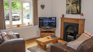 A living room with a fireplace, a television, and a window with curtains. - Four Seasons Cottage (Ambleside)