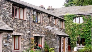 A stone building with a bench outside, a sign reading "Guest House," and a pathway leading to the entrance. - Four Seasons Cottage (Ambleside)