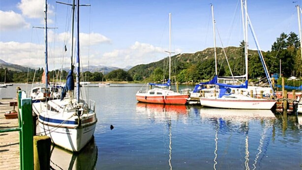 A marina with several sailboats docked, calm water, and a mountainous backdrop. - Four Seasons Cottage (Ambleside)