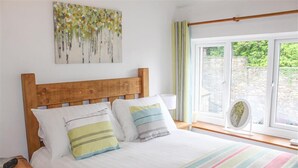 A neatly made bed with striped bedding, a wooden headboard, and a bedside table with a lamp. - Four Seasons Cottage (Ambleside)