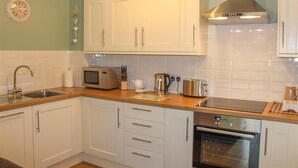 A modern kitchen with white cabinets, a stainless steel range hood, a microwave, a kettle, and an oven. - Four Seasons Cottage (Ambleside)