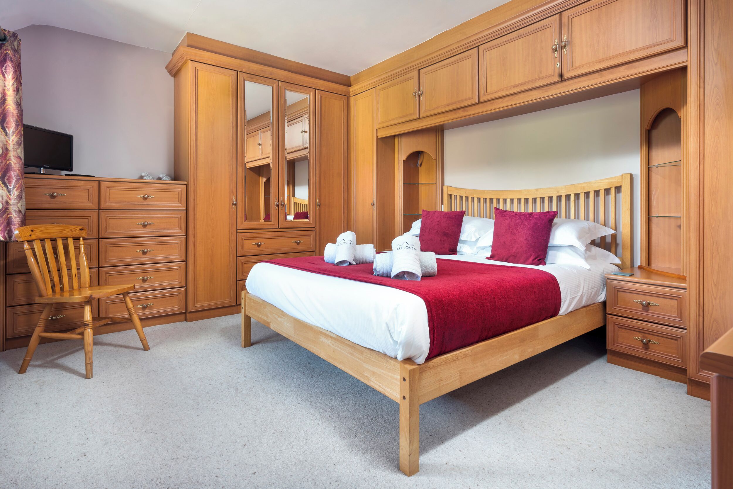 Un dormitorio con cama de madera, una silla, televisor y armarios empotrados.