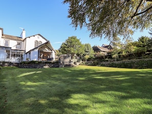 Uma casa grande com um gramado amplo, muros de pedra e um jardim bem cuidado.