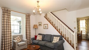 A living room with a grey sofa, a plaid armchair, a wooden coffee table, a staircase, and a window with curtains. - Jessicas Cottage (Windermere)