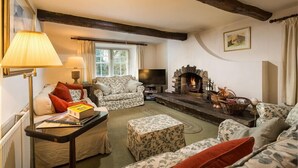 Una sala de estar acogedora con chimenea, un sofá, un televisor y una mesa llena de libros.