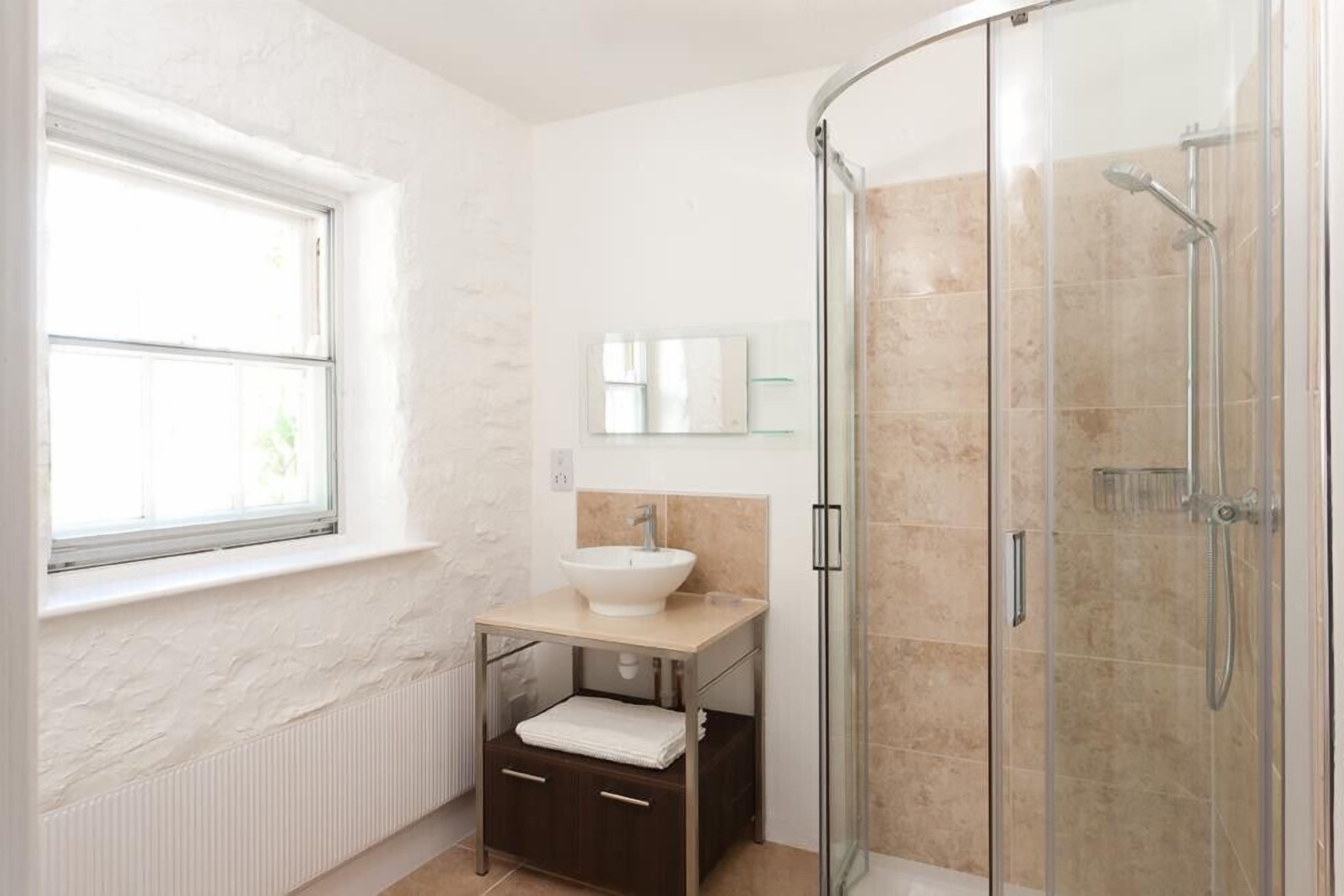 A bathroom with a white sink, a glass shower enclosure, and a window.