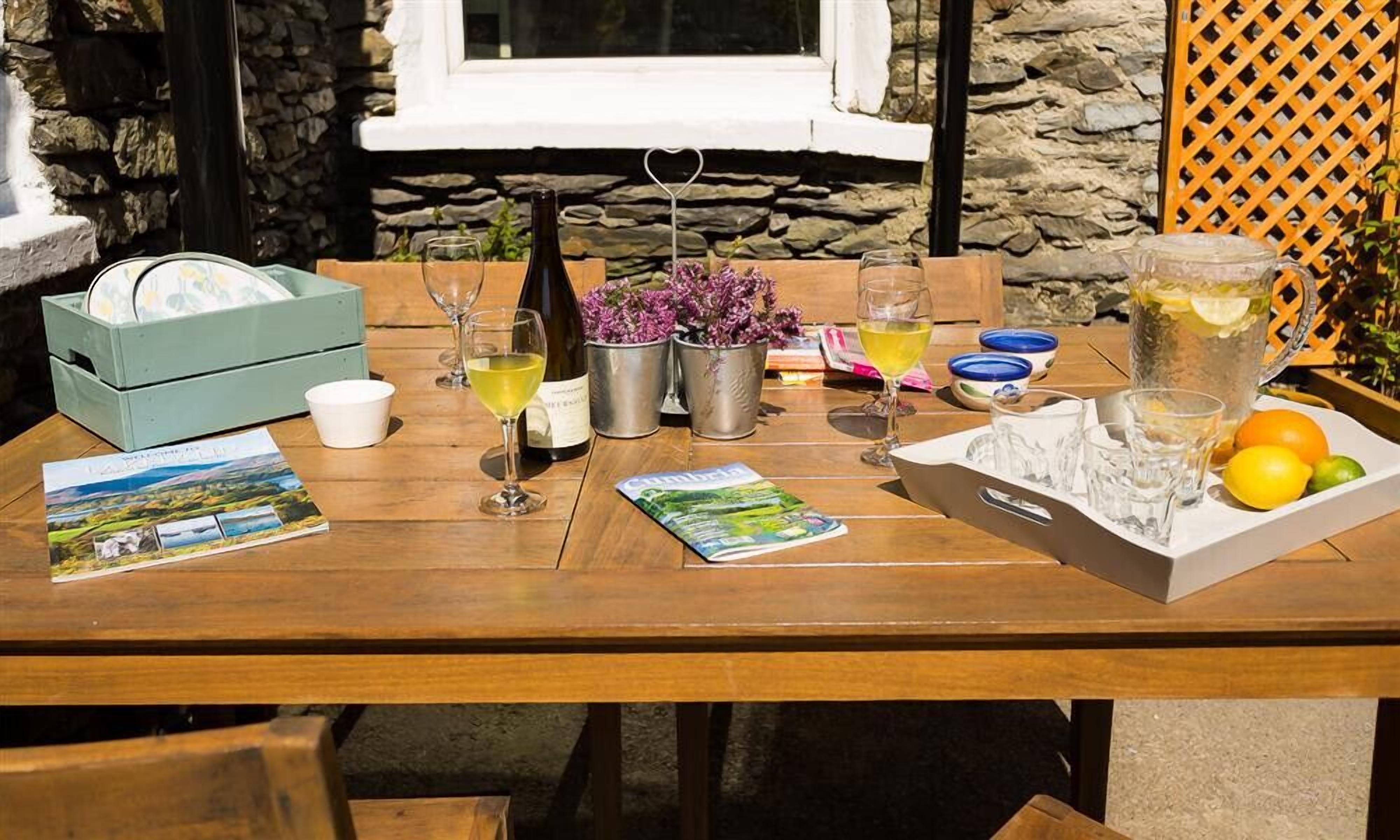 Une table en bois, mise avec des verres à vin, une bouteille, un pichet et un plateau contenant des oranges et des citrons.