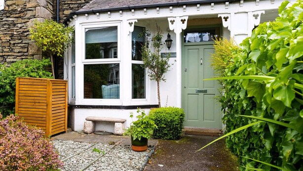 Un affascinante cottage con facciata in pietra, una porta verde e un piccolo giardino con una panchina e piante in vaso.
