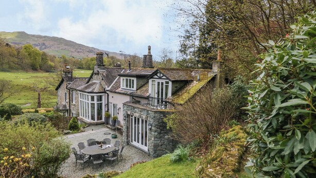 Une maison en pierre dotée d’un patio avec jardin, entourée de verdure et de collines.