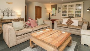 Un salon avec deux canapés, une table basse en bois et un meuble contenant des livres et des objets décoratifs.