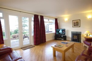 A living room with a television, fireplace, and a view of the outdoors through large windows.