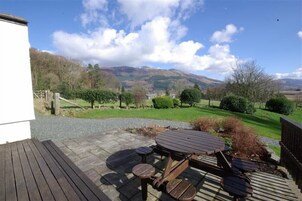 A wooden deck with a picnic table and benches, surrounded by a gravel path and a view of rolling hills and trees.