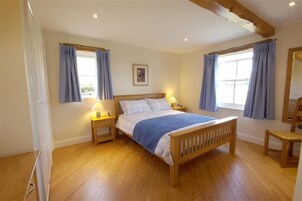 A bedroom with a wooden bed, two bedside tables with lamps, a window with curtains, and a wooden floor.