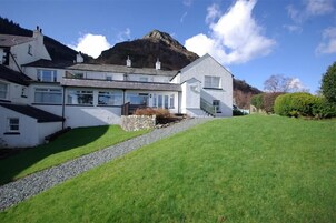 A white building with a stone foundation, a sloped roof, and a view of a mountain in the background.
