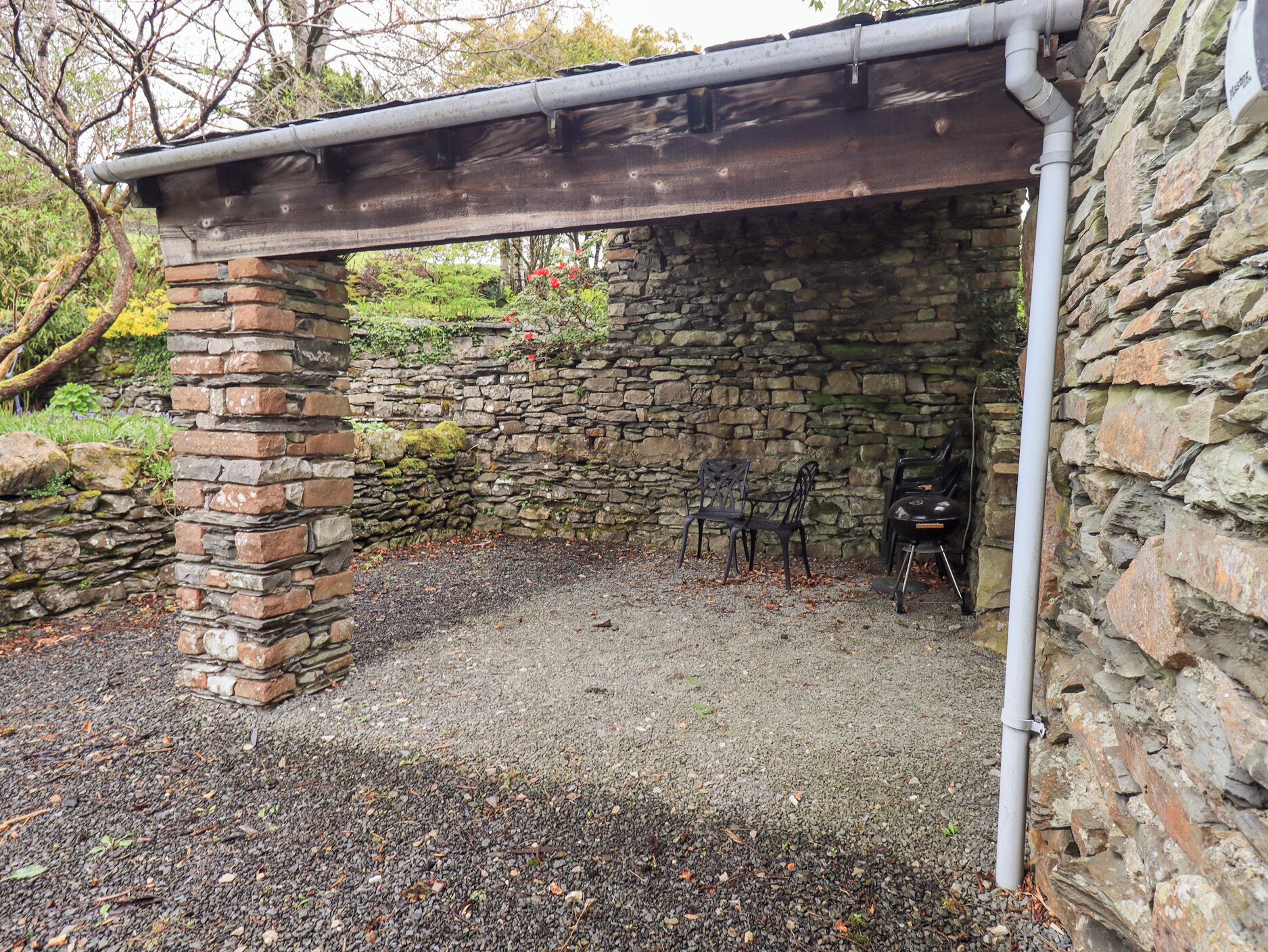 A stone building with a wooden roof structure, a gravel ground, and two black chairs.