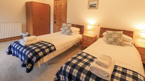 Ein Hotelzimmer mit zwei Betten, jedes mit einer karierten Decke und einem Kopfkissen. Es gibt einen Holzschrank, einen Nachttisch mit einer Lampe und ein gerahmtes Bild an der Wand.