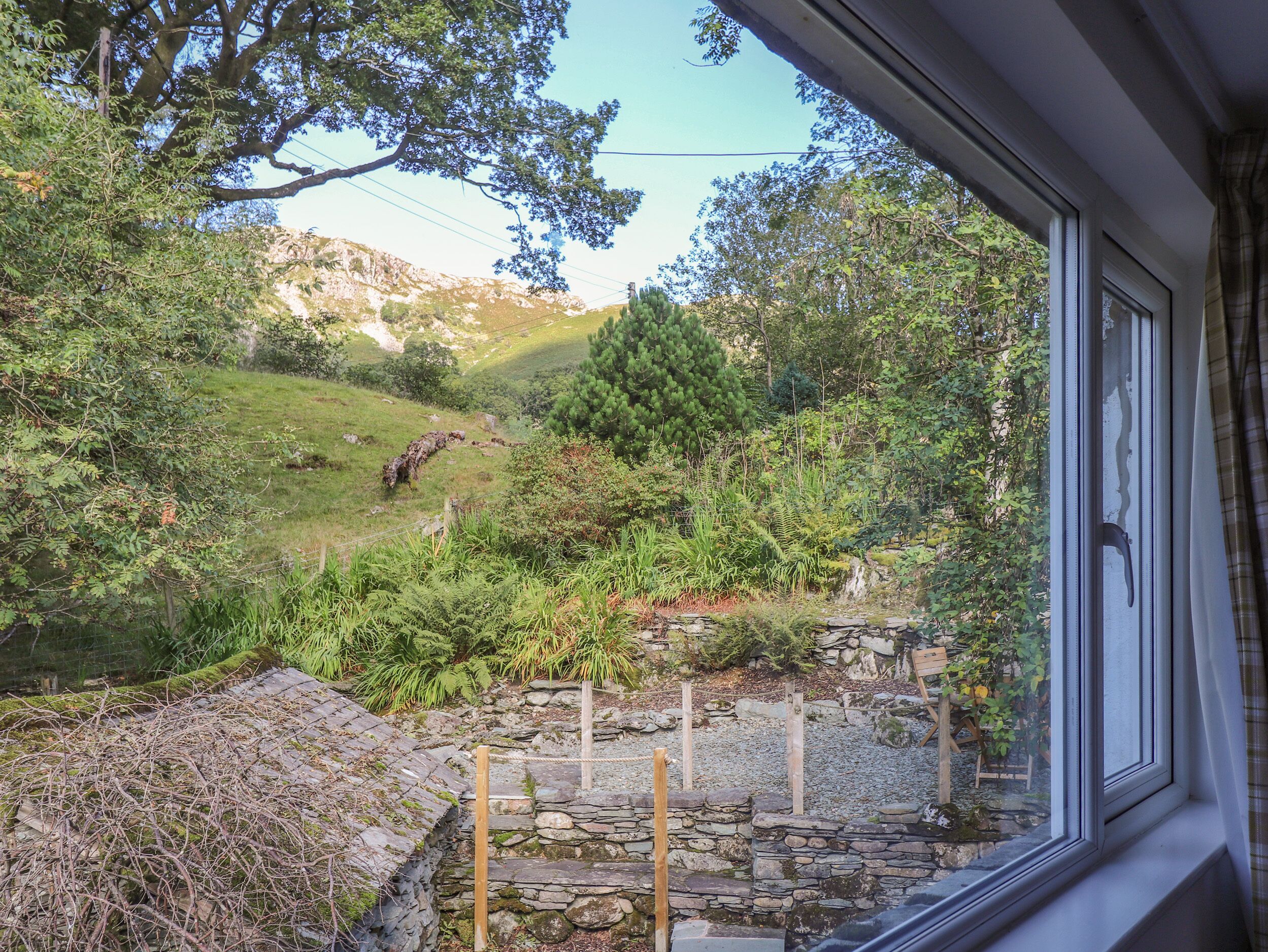 Blick aus einem Fenster auf eine Steinsmauer und einen grasbewachsenen Hügel mit Bäumen.