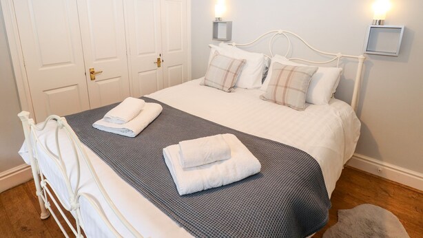 Ein ordentlich gemachtes Bett mit weißen Leinen und einer grauen Decke, ein weißer Metallbettrahmen, ein Holzboden und ein weißer Kleiderschrank mit Messinggriff.