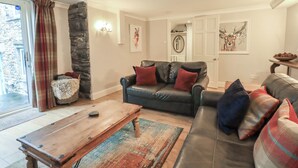 Ein Wohnzimmer mit einer Steinwand, einem schwarzen Ledersofa mit roten Kissen, einem Holztisch und einem farbenfrohen Teppich.