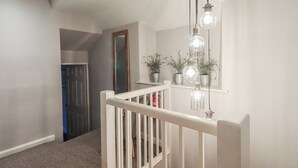 Eine Treppe mit weißer Geländer, eine Hängeleuchte mit mehreren Lampen und eine Tür zu einem weiteren Raum.