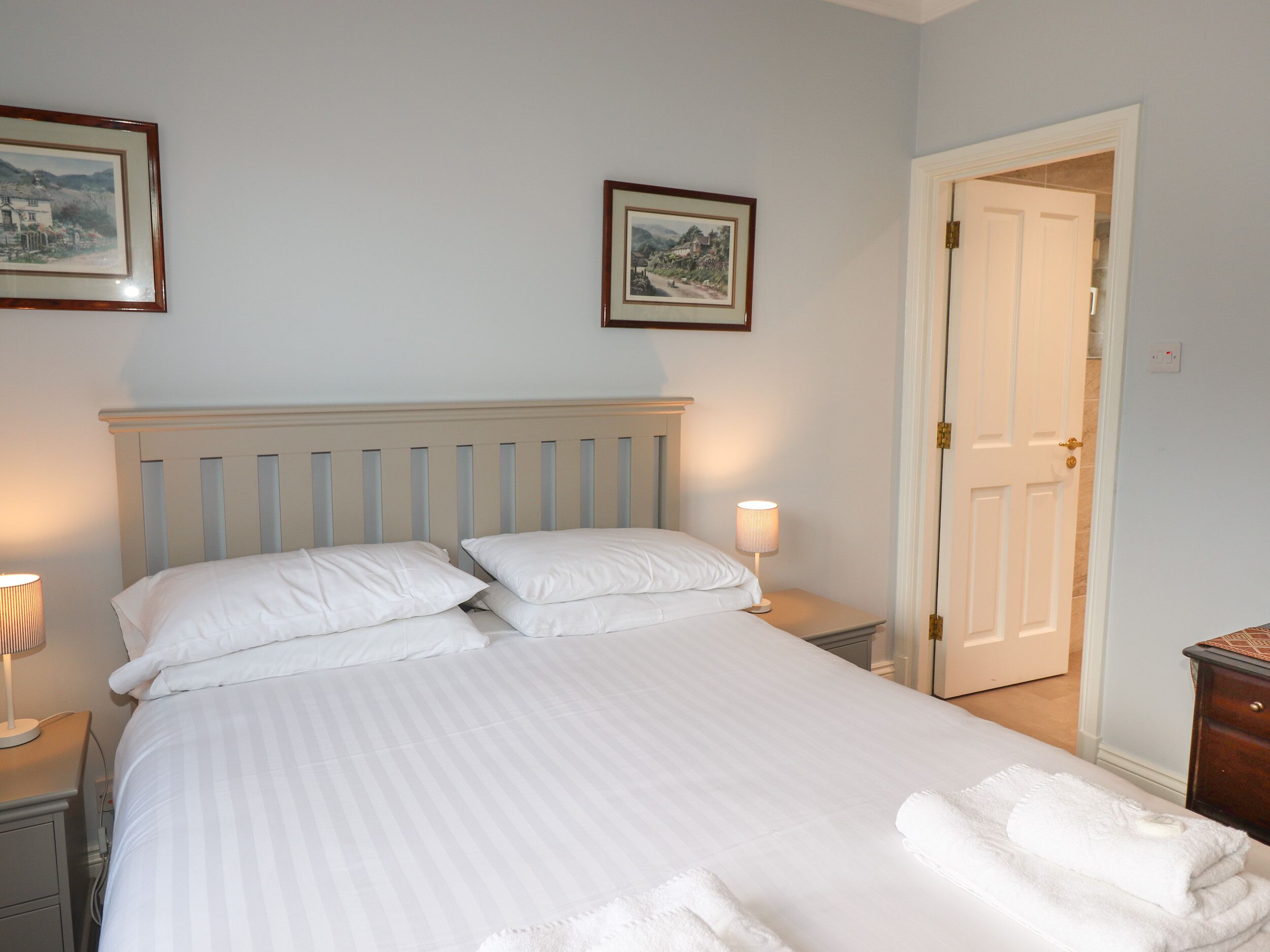 A neatly made bed with white linens and pillows, two bedside lamps, and a door to the right.