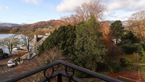 A scenic view of a lake with a castle-like building, surrounded by autumn foliage and hills in the background. - Romney 14 (Ambleside)