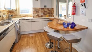 A modern kitchen with a wooden countertop, white cabinets, and a window overlooking a scenic view. - Romney 14 (Ambleside)