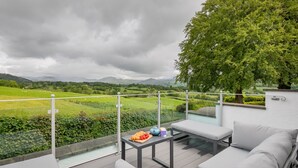 Un balcon donnant sur un paysage verdoyant, une table avec de la nourriture et un espace détente avec des sièges.