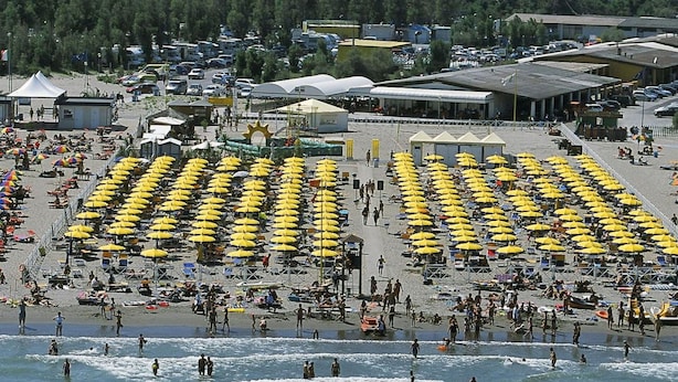 Ein Strand mit Reihen gelber Sonnenschirme und Menschen, die im Wasser schwimmen.