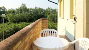 A small outdoor patio with a round table and two white plastic chairs, a brick wall, and a yellow building in the background. - Cosy apartment for 5 people with pool, A/C, WIFI, TV, patio and pets allowed (Rosolina)