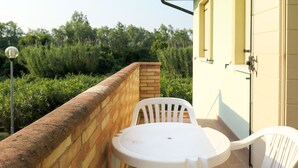 A small outdoor patio with a round table and two white plastic chairs, a brick wall, and a yellow building in the background. - Cosy apartment for 5 people with WIFI, A/C, pool, TV, patio and pets allowed (Rosolina)