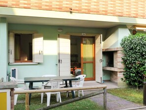 Une terrasse extérieure avec une table et des chaises, un four en briques et un petit coin jardin.