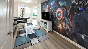 Et værelse med et stort vægmaleri, et hvidt tv-møbel med tv, en sofa og et sofabord.