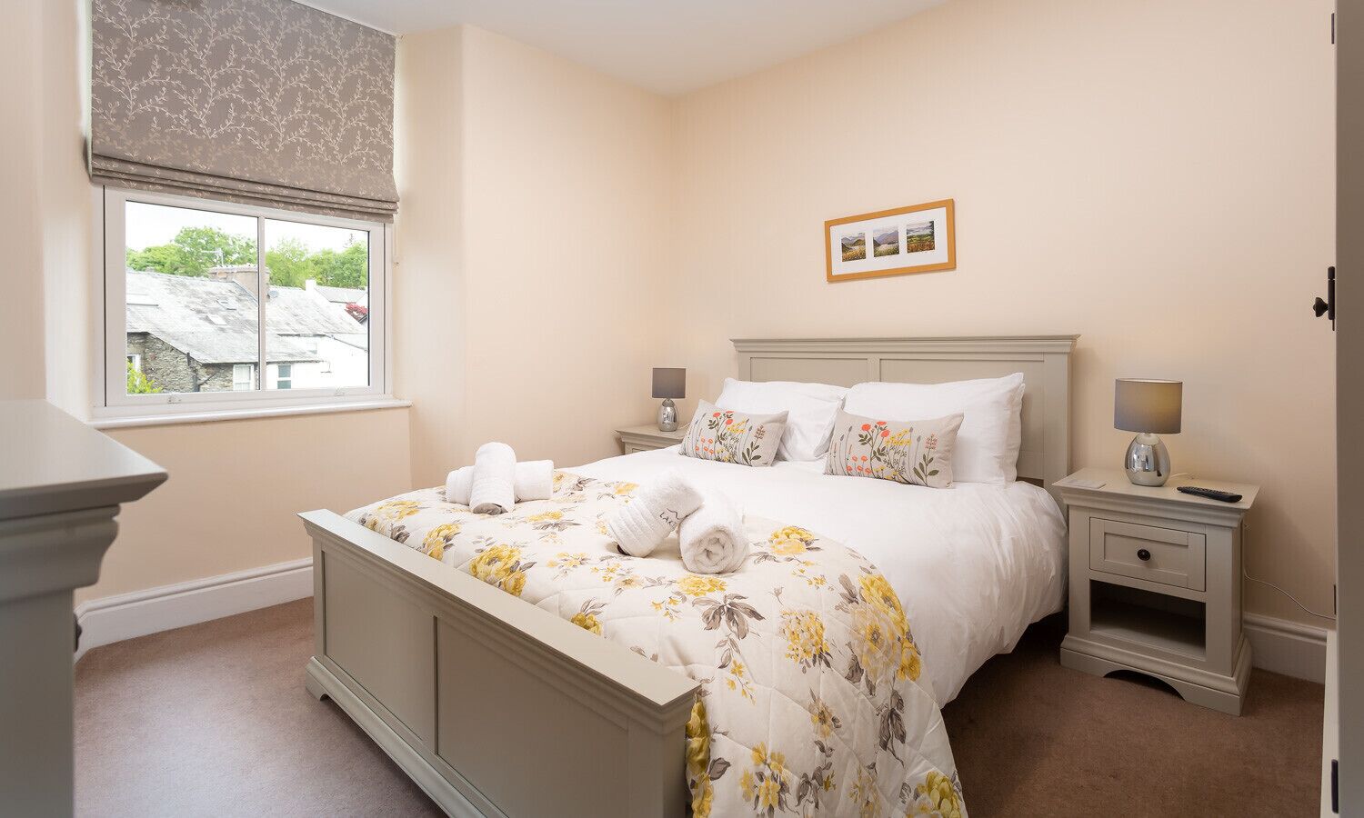 A bedroom with a bed, bedside tables, a window with blinds, and a framed picture on the wall.