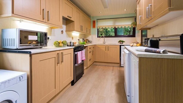A modern kitchen with wooden cabinets, a microwave, a dishwasher, and a window with a view of greenery. - Fairhaven (Windermere)