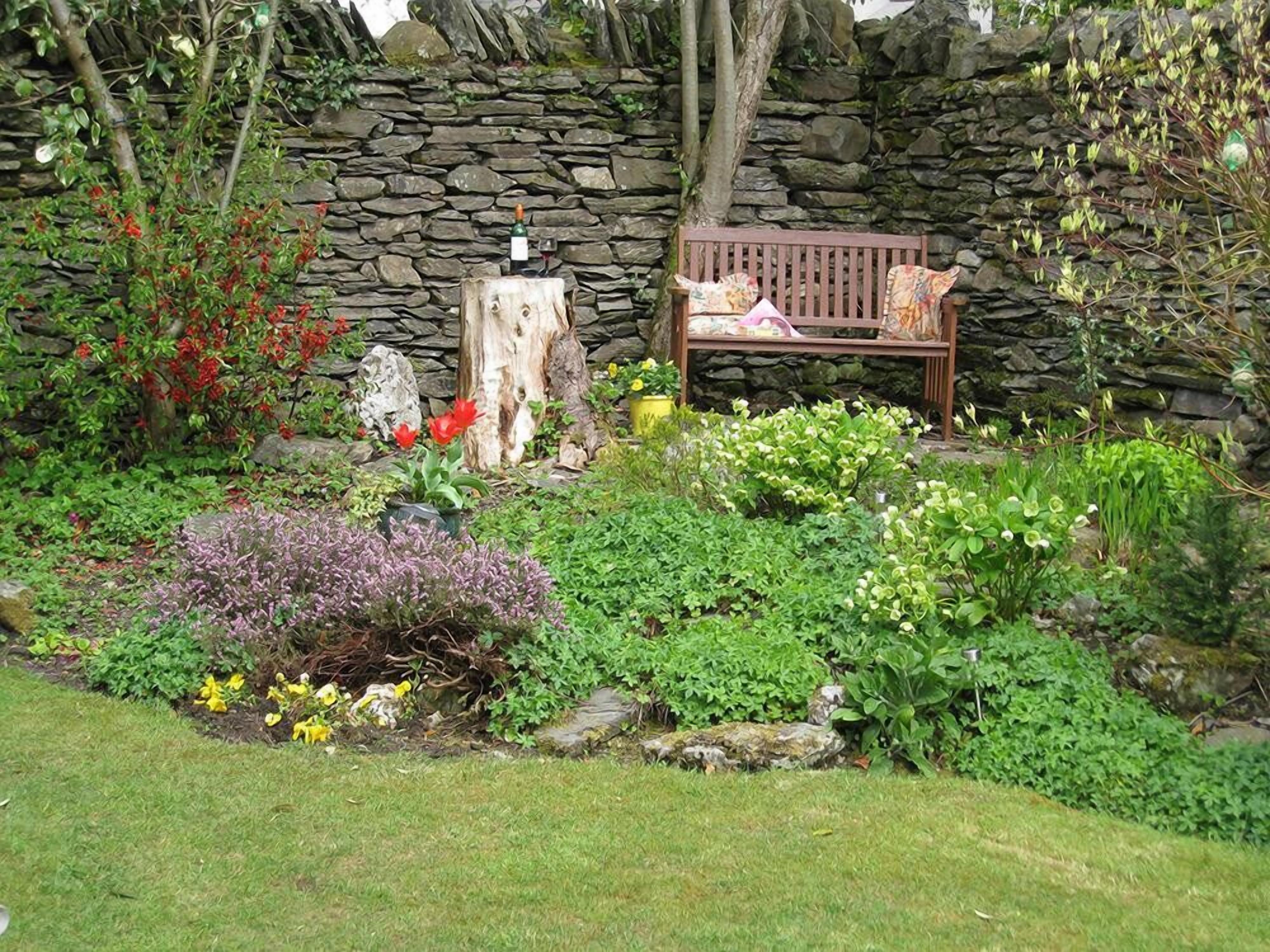 A garden with a stone wall, a wooden bench, and various plants.