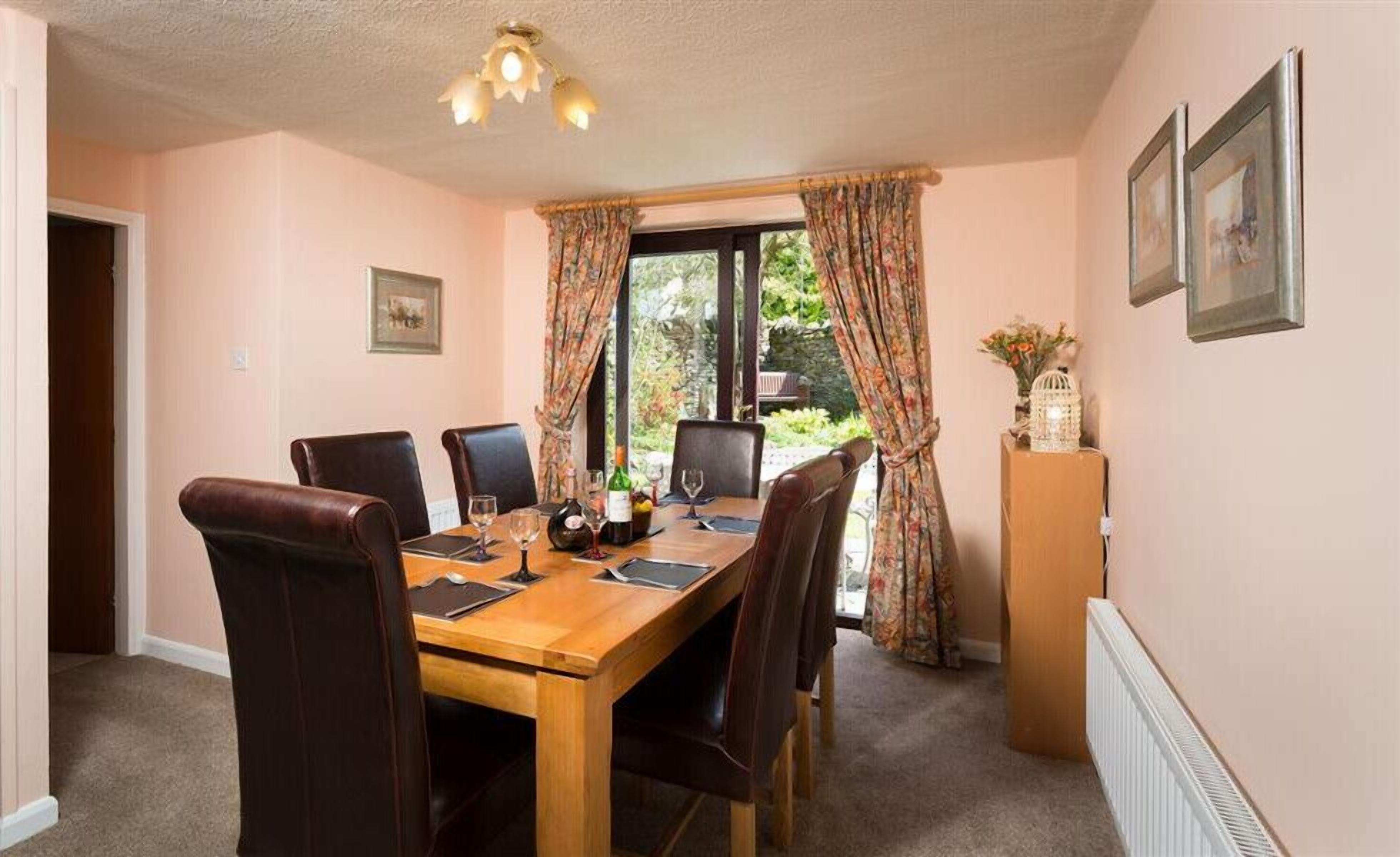 A dining room with a wooden table, six chairs, and a window with curtains.
