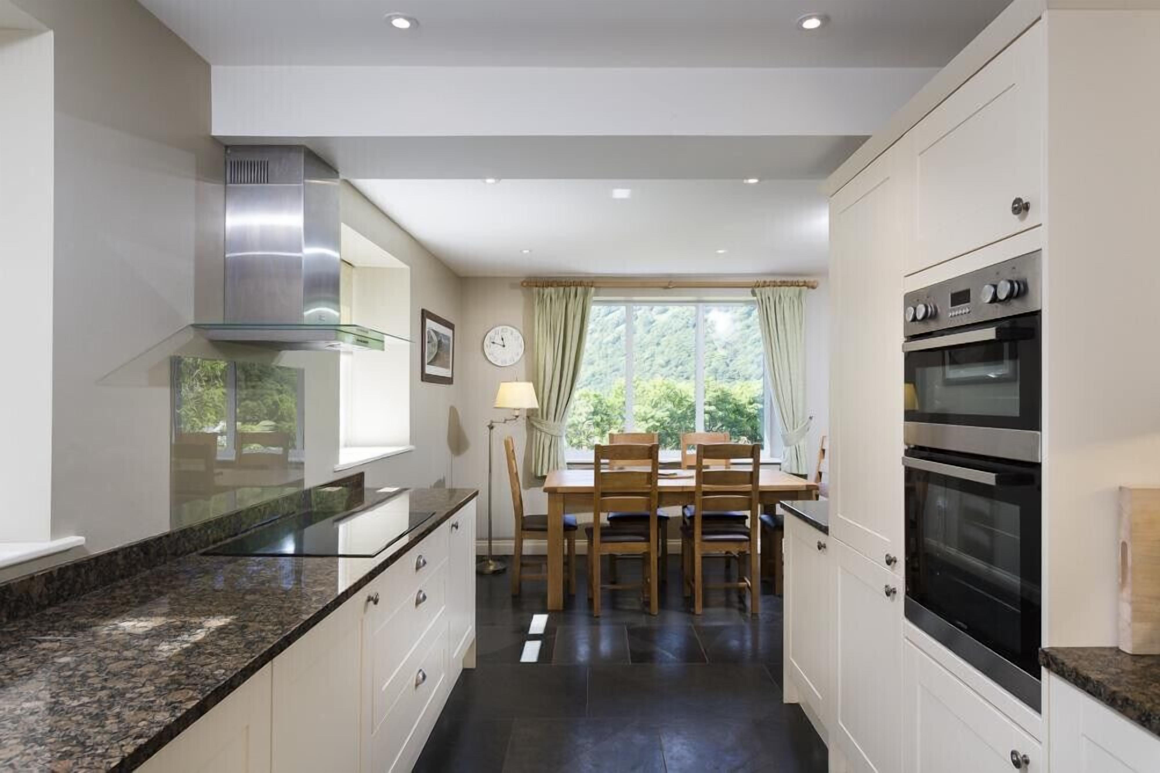 A modern kitchen with granite countertops, stainless steel appliances, and a dining area with wooden chairs and a table.