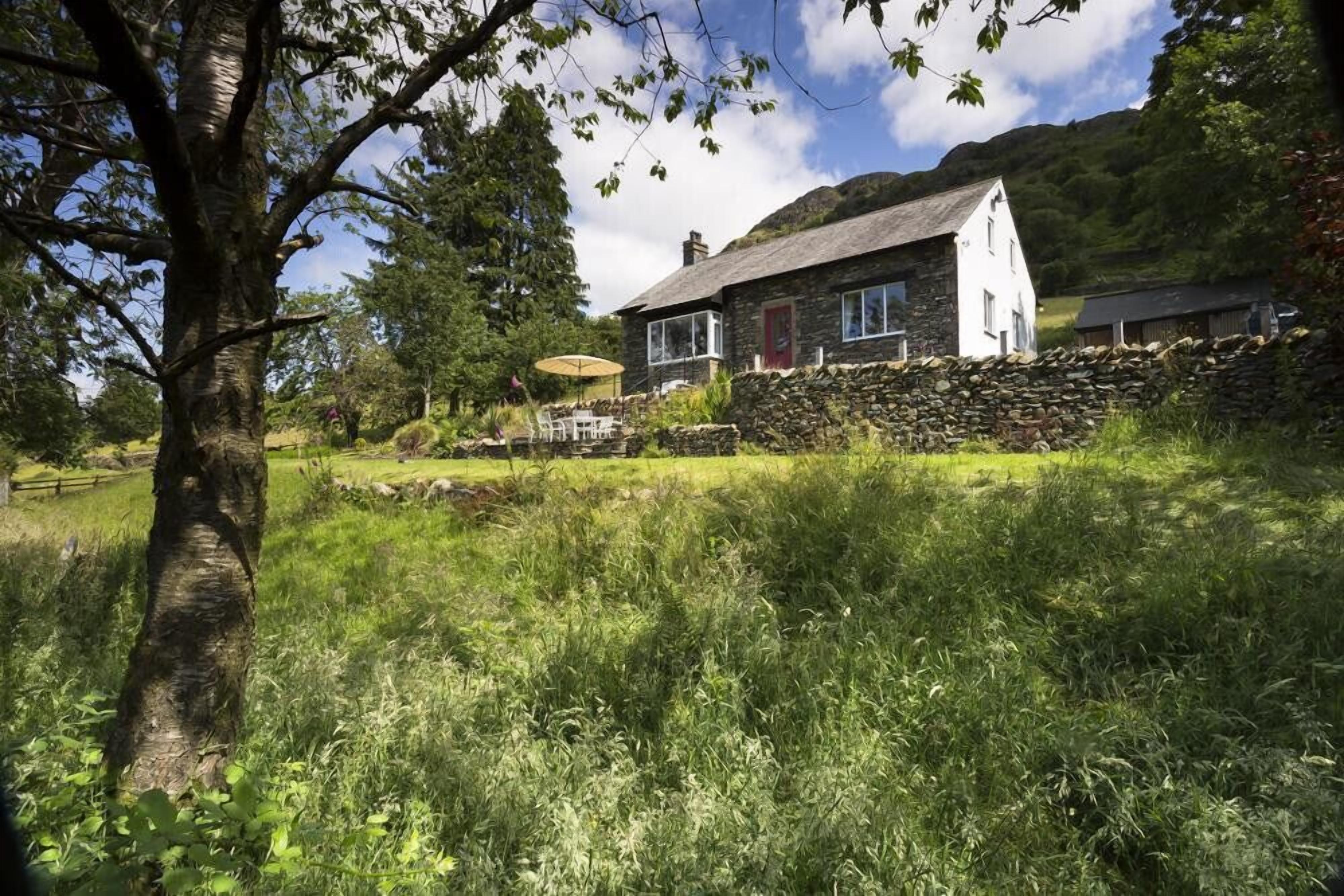 Een stenen huis met een rode deur, omringd door een stenen muur en weelderige begroeiing.