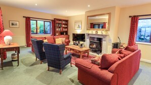 Una sala de estar acogedora con chimenea, sofás rojos, una estantería y un televisor.