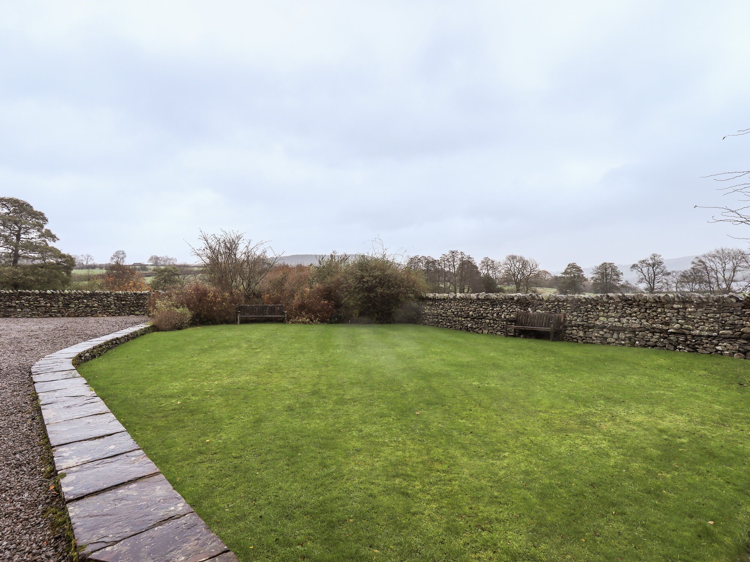 A well-maintained lawn with a stone wall and a bench.