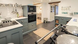 Eine moderne Küche mit integriertem Backofen, Mikrowelle und Kochfeld. Auf dem Boden steht ein kleiner Hocker und eine gewebte Matte.