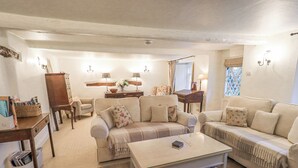 Ein gemütliches Wohnzimmer mit zwei Sofas, einem Couchtisch und einem Beistelltisch. Es gibt einen Holzschrank und einen kleinen Schreibtisch mit einer Lampe.