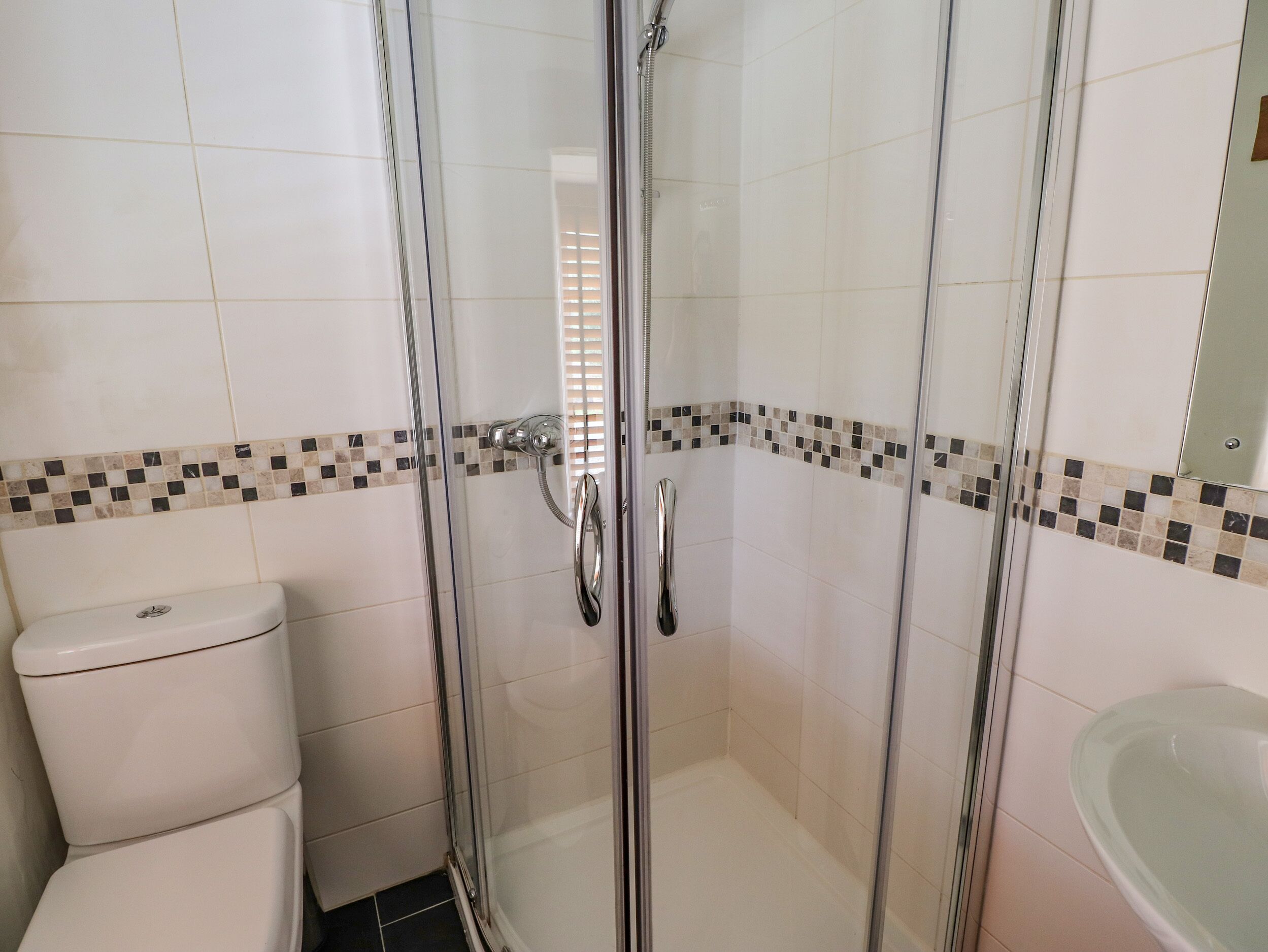 A bathroom with a glass-enclosed shower, a toilet, and a sink.